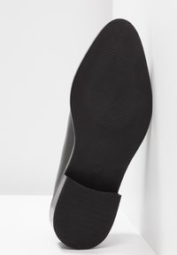 Semelle en cuir noir avec une surface lisse, une forme arrondie et un motif de rainures subtil. Taille 37 indiquée sur le talon.