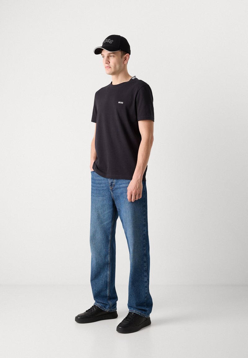 T-shirt en coton noir avec logo "BOSS" blanc, associé à un jean en denim bleu et des baskets noires. La casquette est noire avec un logo brodé blanc.