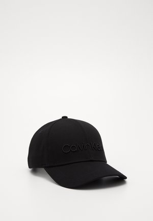 Casquette de baseball noire avec une visière incurvée et un logo en relief "Calvin Klein" brodé sur le panneau avant, placée sur fond blanc.