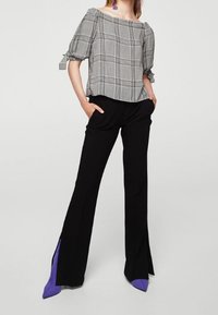 Sorte bukser med lilla spidse detaljer, parret med en grå plaid off-the-shoulder top med puffærmer og bindedetaljer.