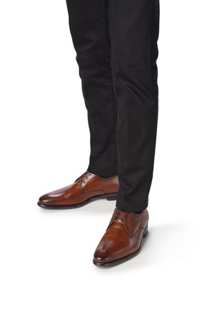 Braune Lederdressschuhe mit Schnürdesign, runder Zehenform und subtiler Textur, kombiniert mit schwarzen Hosen. Glatte Oberfläche und kontrastierende Sohle.