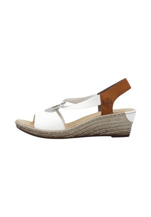 Sandales compensées blanches avec une semelle texturée de couleur naturelle. Elles présentent une sangle d'accent en cuir marron et un cercle décoratif en métal à l'avant.