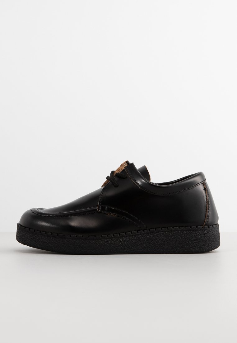 Chaussure en cuir noir à bout arrondi, surface lisse et laçage décoratif ; comprend une semelle en caoutchouc noir texturé.