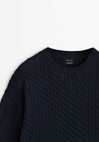 Pull en coton bleu marine à torsades, col rond côtelé et manches longues, plié à plat sur un fond blanc.