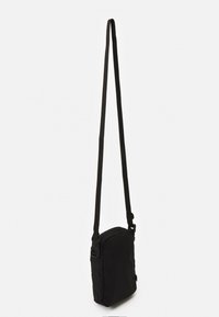 Borsa crossbody nera di piccole dimensioni con lunga tracolla regolabile appesa su sfondo bianco.