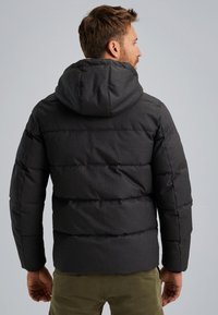 Čierna prešívaná bunda s kapucňou, s prešívaným dizajnom, hladkou textúrou a jemným leskom. Zadná strana ukazuje uvoľnený strih a detaily šitia.