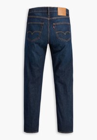 Mörkblå denimjeans med rak ben-design, synlig sömnad, två bakfickor och en tan läderlapp vid midjan.