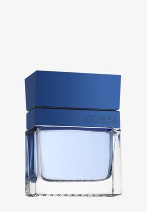 Przezroczysta prostokątna szklana butelka z jasnoniebieskim płynem i dużą ciemnoniebieską prostokątną nakrętką, z napisem "GUESS" na froncie.