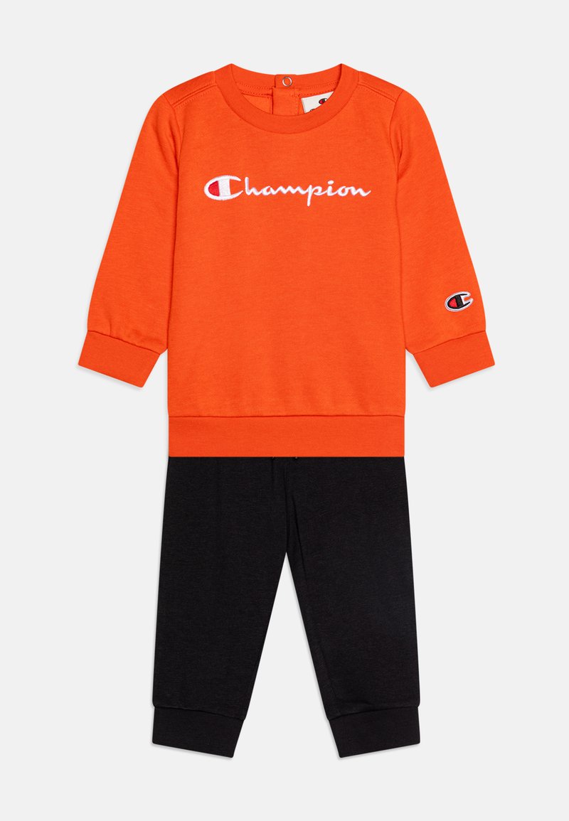 Sudadera naranja con el logo blanco de "Champion" y pantalones negros. Presenta mangas largas, puños acanalados y un diseño tonal para mayor comodidad.