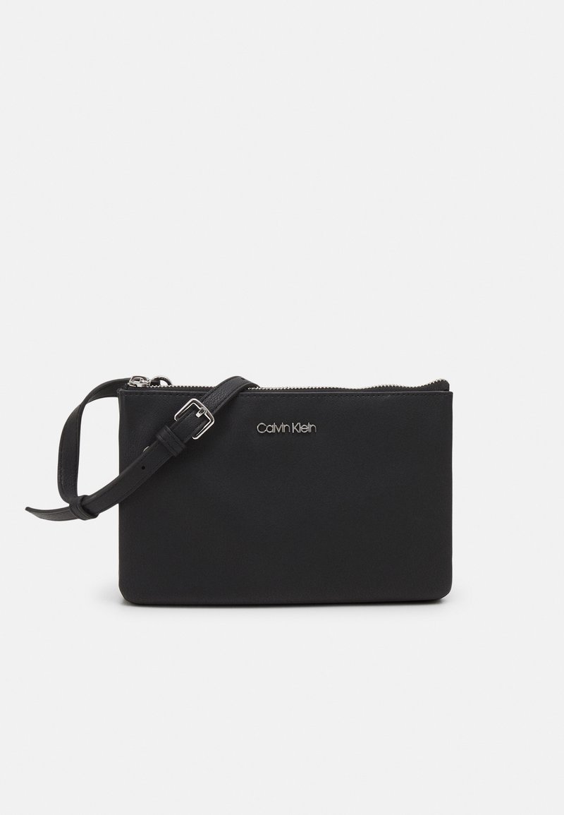 Schwarze Clutch aus glattem Material mit Reißverschluss, verstellbarem Schultergurt und metallic Logo. Kompakte rechteckige Form.