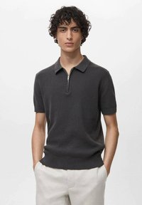 Polo shirt scurt, de culoare gri închis, cu un model texturat, având guler cu fermoar și manșete ribbed, asortat cu pantaloni de culoare deschisă.