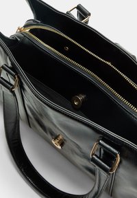 Sac à main en cuir noir avec des zips dorés, compartiments intérieurs et fermeture à pression magnétique. Dispose de poignées solides et d'une texture lisse.