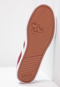 Podeszwa bordowych sneakerów z białymi wykończeniami, z wzorem podeszwy w jodełkę, logo Hummel oraz stylizowanym symbolem pszczoły na pięcie.