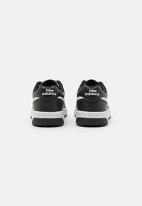 Baskets en cuir noir avec accents blancs, dotées d'une semelle en caoutchouc et du logo "New Balance" sur le talon. Design arrondi avec une texture lisse.