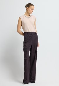 Top sin mangas color rosa claro con cuello adornado, combinado con pantalones de tiro ancho a rayas moradas oscuros que tienen bolsillos laterales.