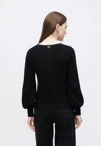 Camisola preta de malha com uma silhueta ajustada, mangas largas e decote redondo. Apresenta um pequeno detalhe dourado nas costas.