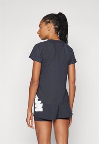 Camiseta atlética azul-escura de mangas curtas, tecido texturizado, gola redonda e costas com hem ajustado, combinada com calções pretos que apresentam um logótipo branco.