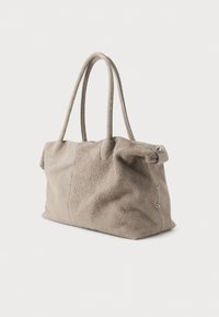 Beżowa torba na ramię z zamszu z dwoma solidnymi uchwytami, miękkim kształtem, widocznym przeszyciem i srebrnymi zdobieniami po bokach.