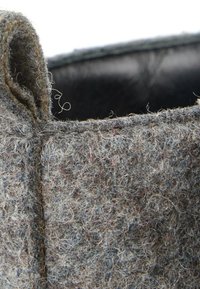 Gros plan d’un tissu feutré gris texturé avec un détail en boucle et des fibres visibles, montrant une partie d’un matériau doux et épais.