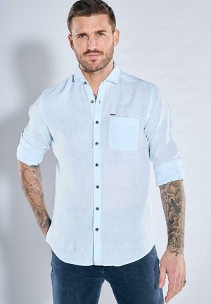 Helles blaues Leinenhemd mit Button-Down-Kragen, Brusttasche und schwarzen Knöpfen; lange Ärmel hochgekrempelt und strukturiertes Gewebe.