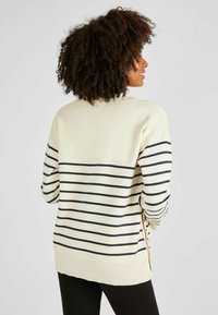 Cremefarbener Sweatshirt mit gestreiften navy Linien, seitlichen Schlitzen und Knopfdetails, geripptem Saum und einer lockeren Passform.