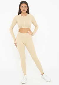 Completo activewear beige a costine composto da un crop top a maniche lunghe con scollatura rotonda e leggings a vita alta, entrambi con una texture liscia.