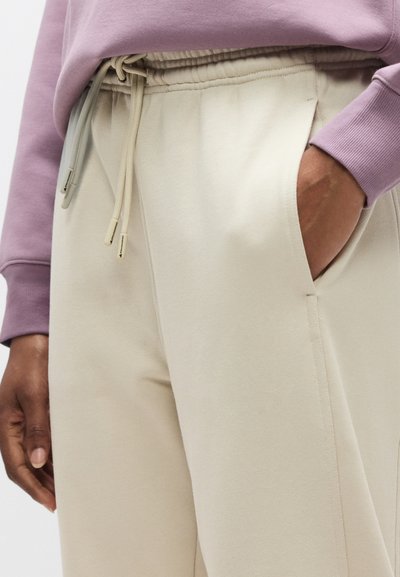 Μπεζ παντελόνι jogging με απαλή υφή, ελαστική μέση και κορδόνια. Συνδυασμένο με ανοιχτό μωβ φούτερ, μερικώς ορατό.