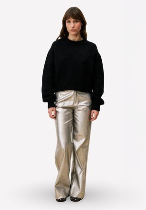 Zwarte cropped trui met een pluizige textuur, gecombineerd met glanzende, metalen zilveren wijd uitlopende broek. De outfit wordt compleet gemaakt met zwarte schoenen.