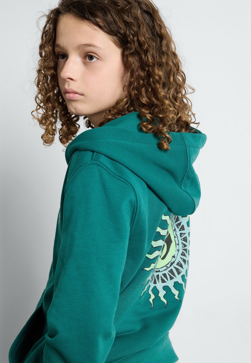 Felpa teal con una consistenza morbida, caratterizzata da un grande design grafico sul retro in verde e nero, e un cappuccio regolabile con cordino.