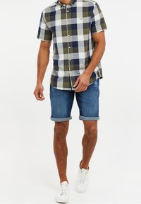 Maglietta a maniche corte a quadri in bianco, blu navy e verde. Abbinata a pantaloni corti di denim blu, con risvolti, e sneakers bianche. Logo in evidenza.