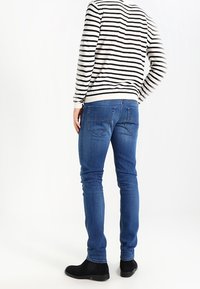 Slim-fit blå denimjeans med fem fickor; bärs med en svart och vit randig tröja och svarta ankelboots.