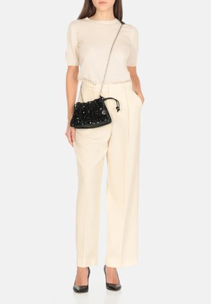 Borsa a tracolla nera con perline, top corto a maniche corte color crema e pantaloni larghi beige chiaro con pieghe. Tacchi alti neri.