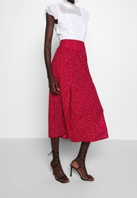 Blouse blanche à volants avec une texture à pois associée à une jupe rouge mi-longue à pois blancs ; sandales à talons noires à lanières.