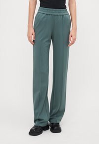 Ljusgröna, vida byxor gjorda av mjukt material med resårmidja. Har vertikala sömmar och en slät yta.