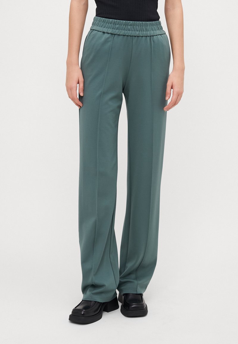 Ljusgröna, vida byxor gjorda av mjukt material med resårmidja. Har vertikala sömmar och en slät yta.