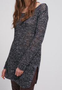 Överdimensionerad, löst stickad tröja i mörkgrå med en fyrkantig form, bred halsringning och sidofickor. Har en texturerad, lager-på-lager garndesign.