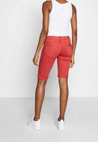 Punaiset farkkushortsit, joissa on käännetyt reunukset, kaksi takataskua ja vetoketjusomiste. Yhdistetty valkoiseen ribbineulottuun topiin ja valkoisiin tennareihin.