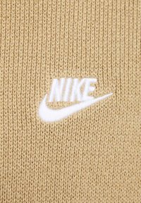 Beige stickad tyg med en vit broderad Nike-logotyp centrerad på materialet.