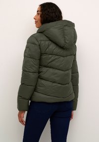 Veste rembourrée vert olive avec une capuche, présentant des sections matelassées horizontales, une texture lisse et un petit logo sur le bras gauche.