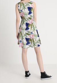 Sukně bez rukávů s květinovým vzorem v krémové barvě, s modrými motýly a růžovými květy. Elastický pas a sukně s volným střihem.