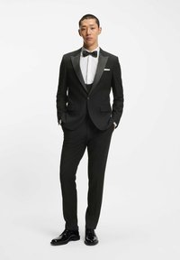 Tuxedo nero con rever in raso, camicia bianca e papillon. Design slim-fit, texture morbida, completato da eleganti scarpe nere lucide.