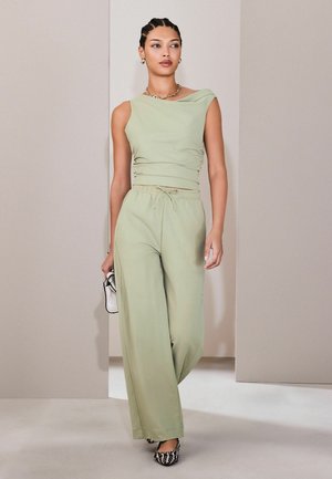 Hellgrünes ärmelloses Oberteil mit asymmetrischem Ausschnitt, kombiniert mit lockeren, passenden Hosen. Mit lockerem Schnitt und weichem Stoff.