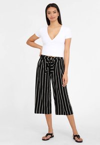 Valge lühikeste varrukatega top V-kaelusega, sobitatud must-valgete triibuliste culottidega, millel on nöörvöö ja laiade jalgadega lõige. Mustad plätud.