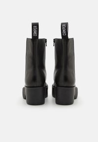 Black leather ankle boots with a block heel, side zippers, and fabric pull tabs. Smooth texture and minimalistic design.