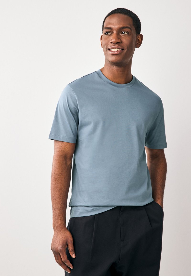 Lichtblauw T-shirt met korte mouwen in een gladde stof en een ronde hals, gecombineerd met een donkere broek. Eenvoudig ontwerp, zonder zichtbare patronen of logo's.