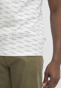 Valge T-särk sinise tekstiga, kus kordub "CASUAL FRIDAY", koos oliiv roheline pükste ja juhusliku disainiga.