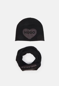 Berretto in maglia nera con una grafica a cuore e "HUGO" in materiale lucido, abbinato a una sciarpa infinita nera con lo stesso logo.