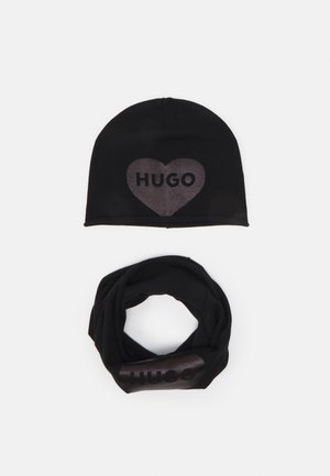 Zwarte gebreide beanie met een hartgrafiek en "HUGO" in glanzend materiaal, gecombineerd met een zwarte infinity sjaal met hetzelfde logo.