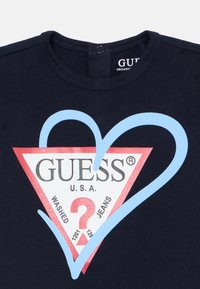 T-shirt en coton bleu marine avec un graphique en forme de cœur rouge et bleu clair portant « GUESS U.S.A. » et un texte sur une étiquette contrastante blanche.