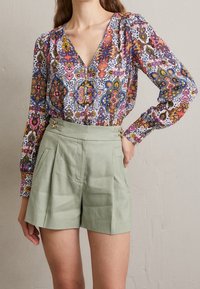 Multikleurige blouse met een patroon, lange mouwen en een V-hals, gecombineerd met lichtgroene shorts met plooien en gouden hardware accenten.